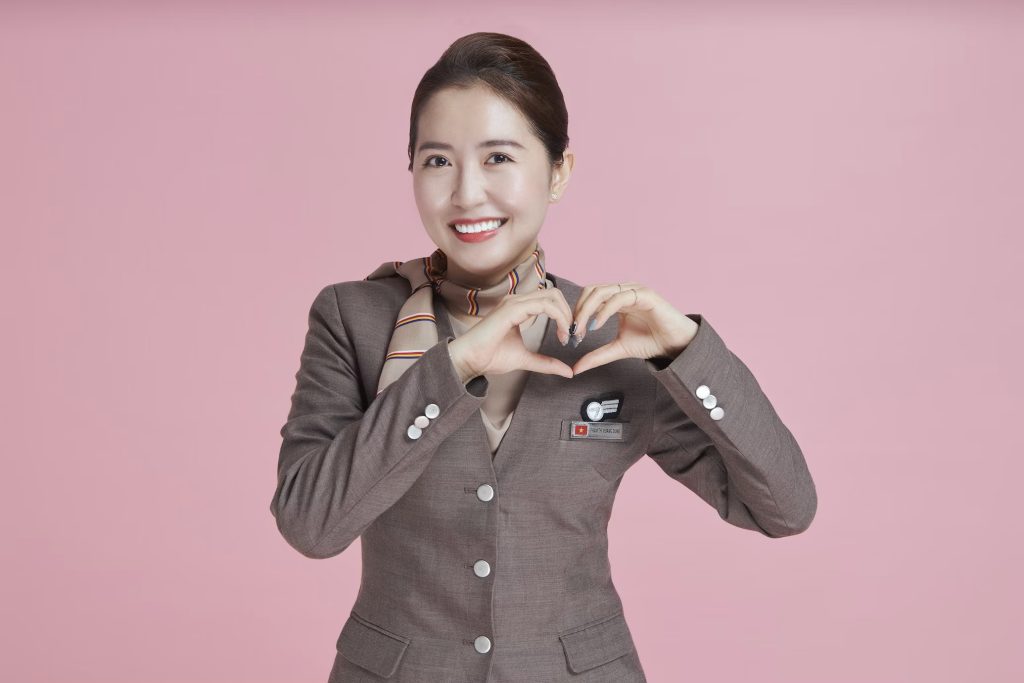 Das Bild zeigt eine emotionale, freundliche, zugewandte Stewardess, die mit ihren Händen ein Herz formt.